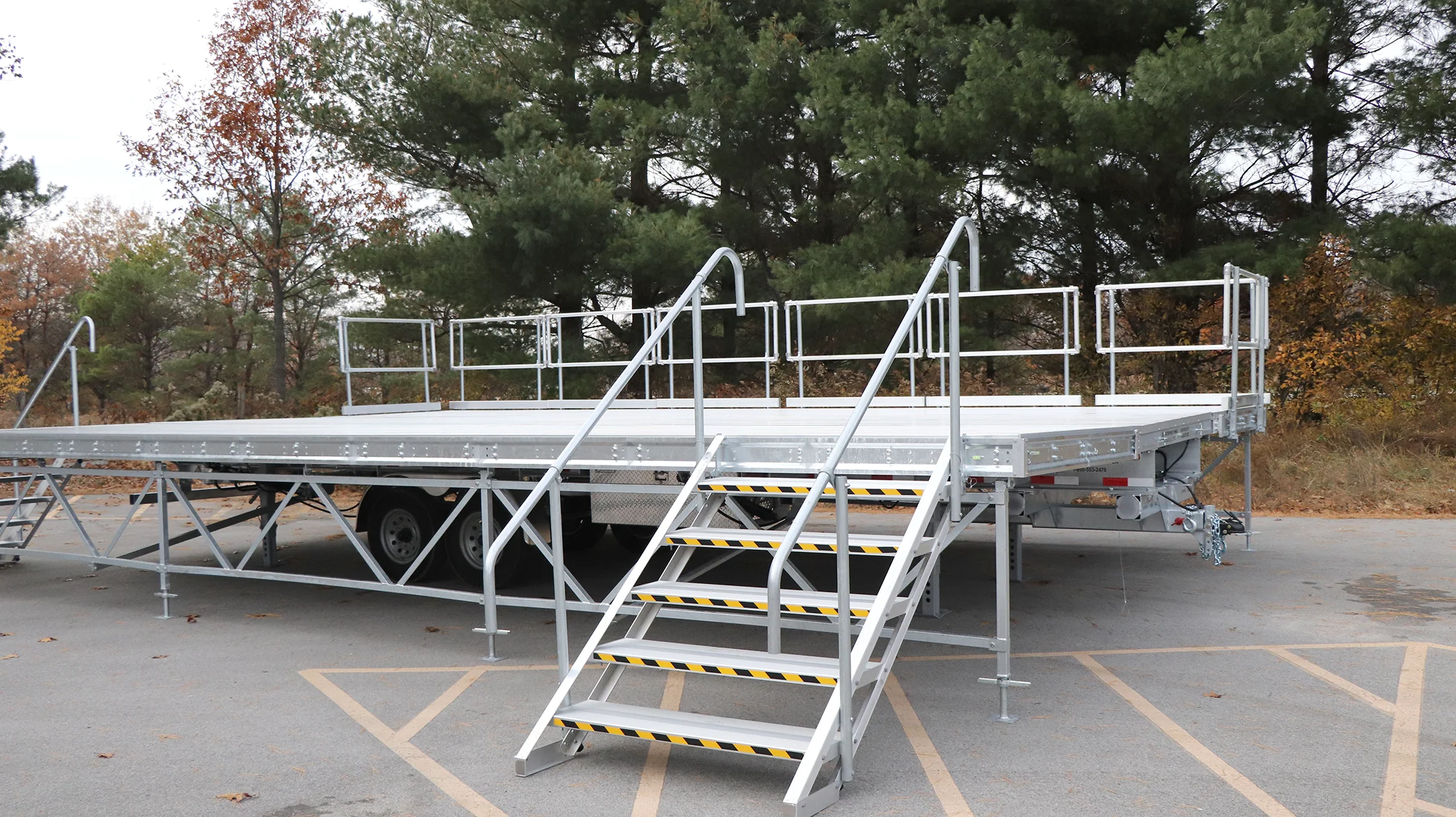 Metal platform trailer with stairs and handrails in a parking lot.