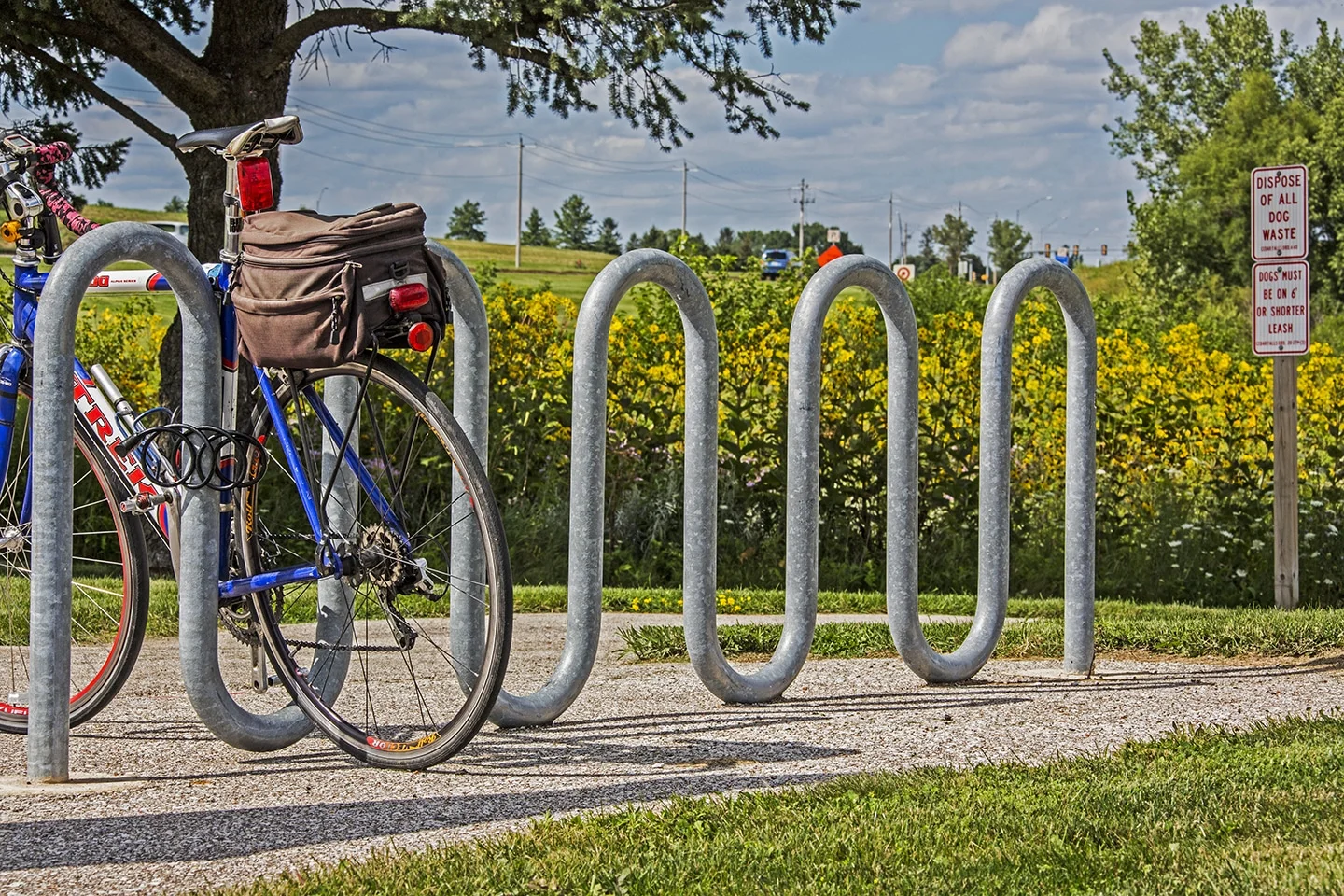 Bicycle parked in a bike rack near a field and sign.