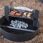 Portable grill with food cooking on top and rocks in bottom.