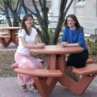 Two women sitting at a red picnic table outdoors.