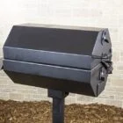 Black electric grill on a stand in front of a brick wall.