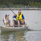 Man paddling kayak with dog in front.