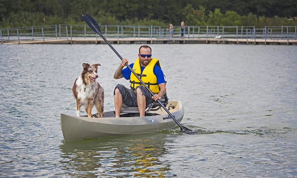 Man paddling kayak with dog in front.