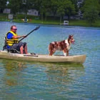 Man paddling kayak on lake with dog standing in front.