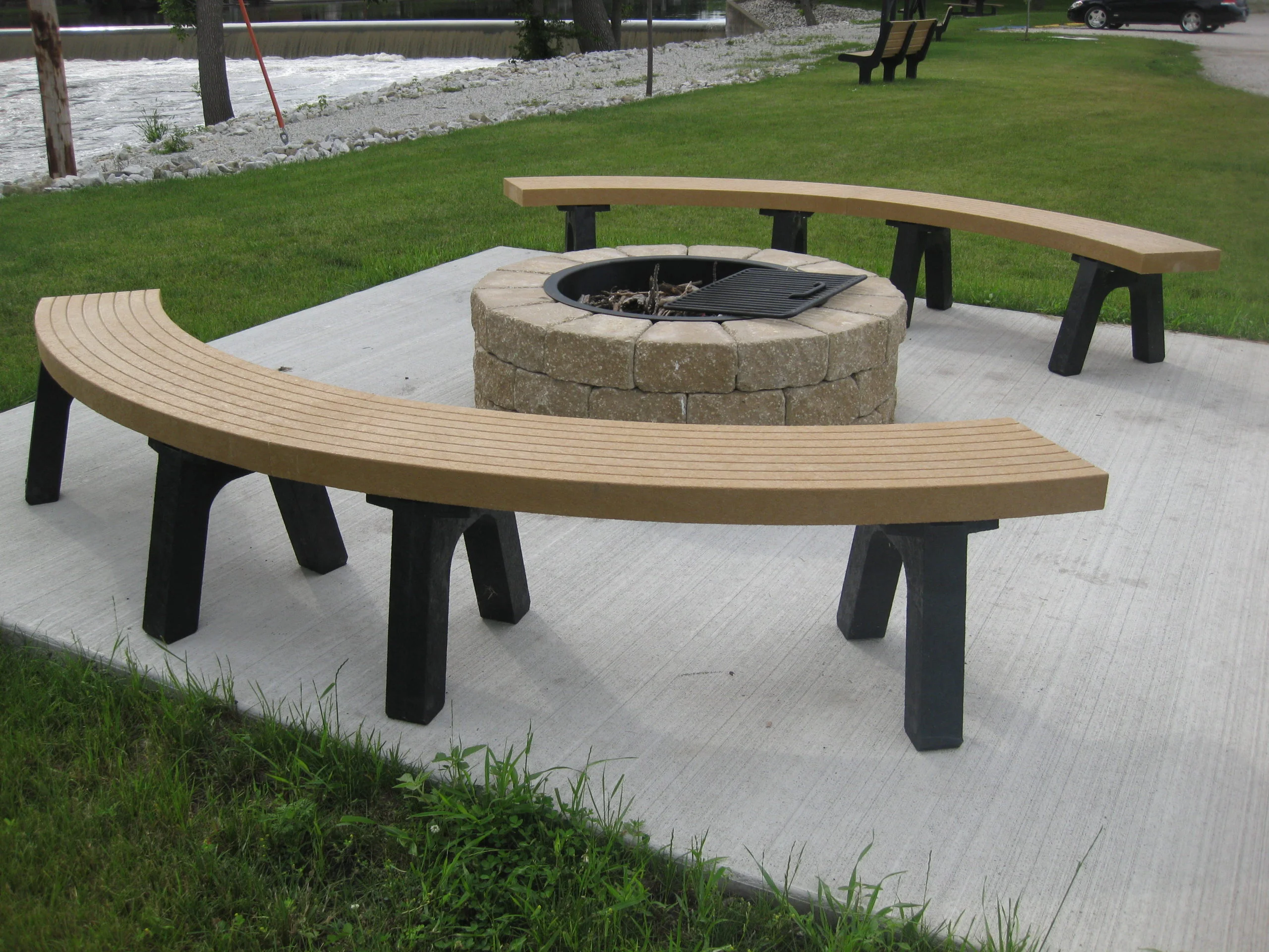Outdoor curved bench and fire pit in a park setting.