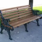 Wooden bench with black metal armrests and legs on a sidewalk.