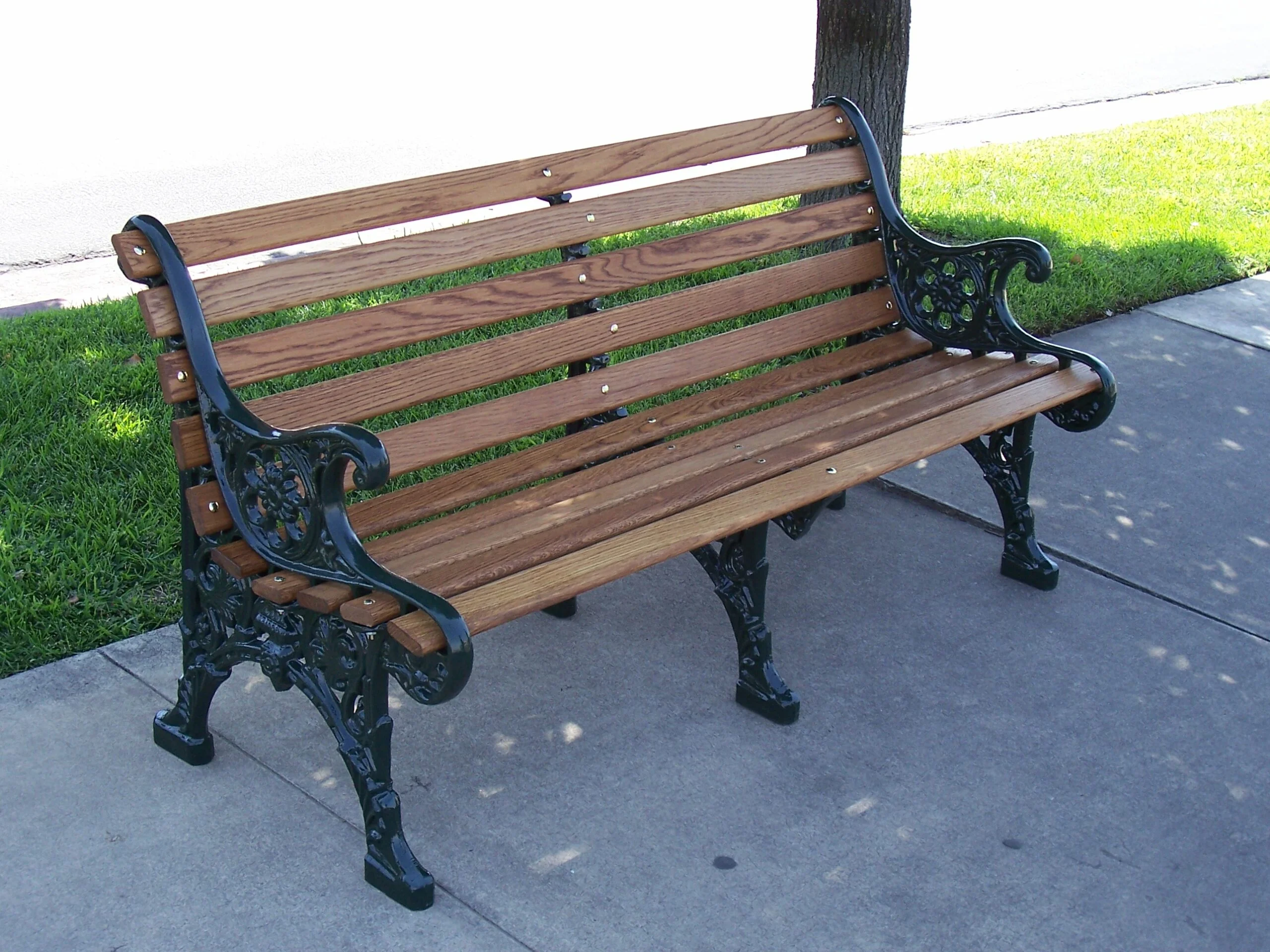 Wooden bench with black metal armrests and legs on a sidewalk.
