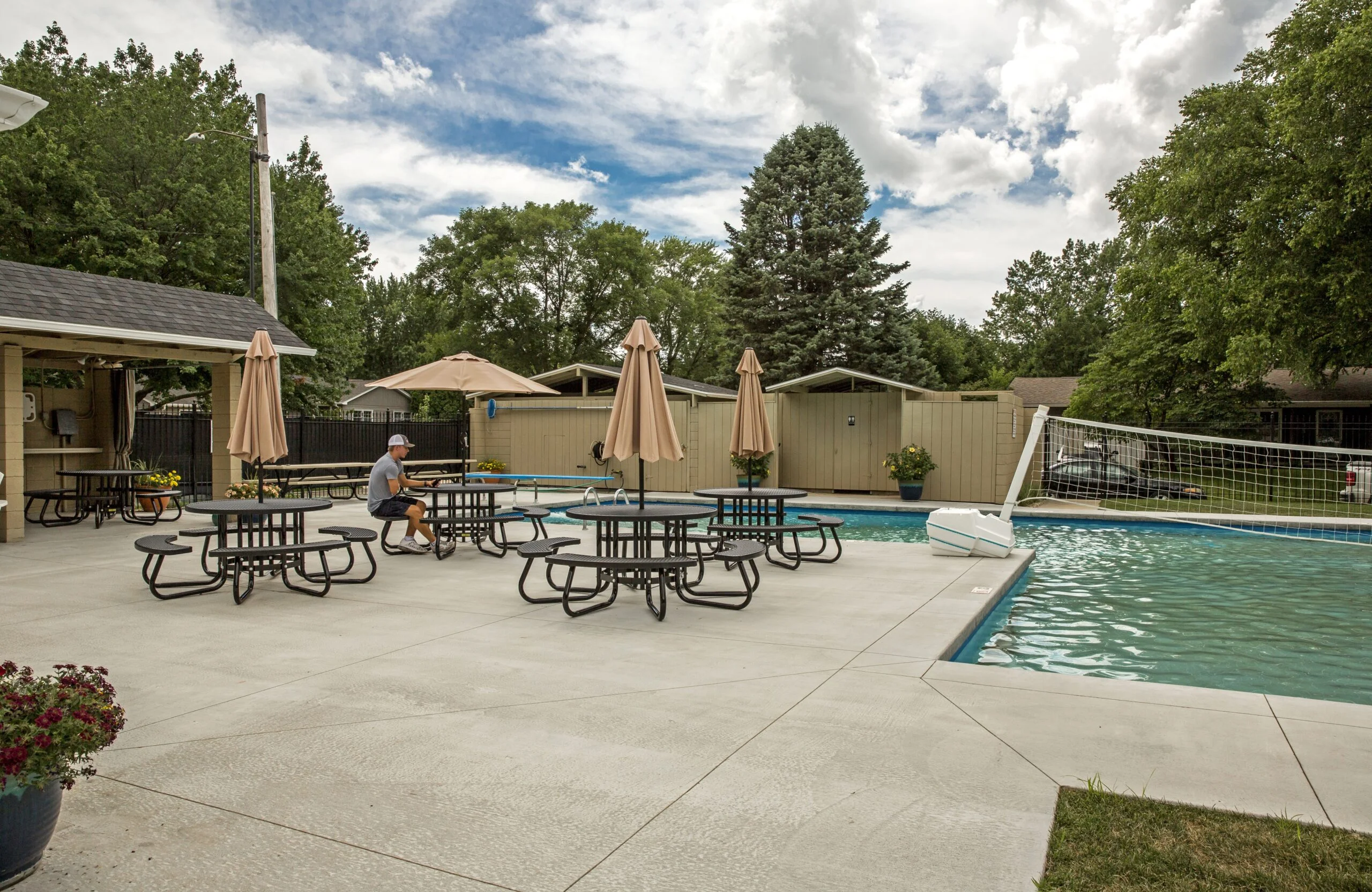 Poolside picnic area with tables and umbrellas near a swimming pool.