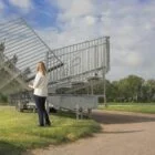 Woman standing next to a large metal structure on grass.