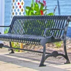 Black metal park bench in front of a blue wall and plants.
