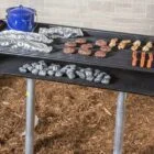 Outdoor grill with charcoal and food cooking on a tabletop.