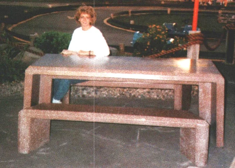 Woman standing behind a large stone table in an outdoor setting.