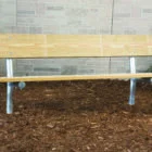 Wooden bench on mulched ground against brick wall.