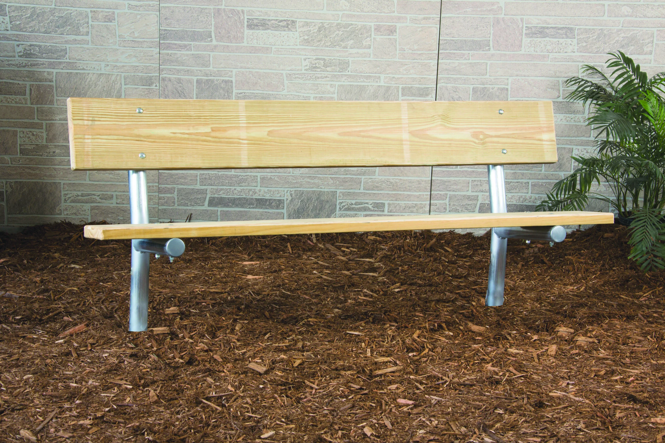 Wooden bench on mulched ground against brick wall.