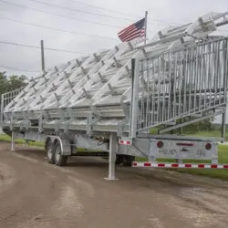 A trailer carrying a stack of metal bleachers on a dirt road.