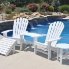 White Adirondack chairs and side table by a pool.