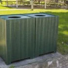 Green trash bin in a park setting.