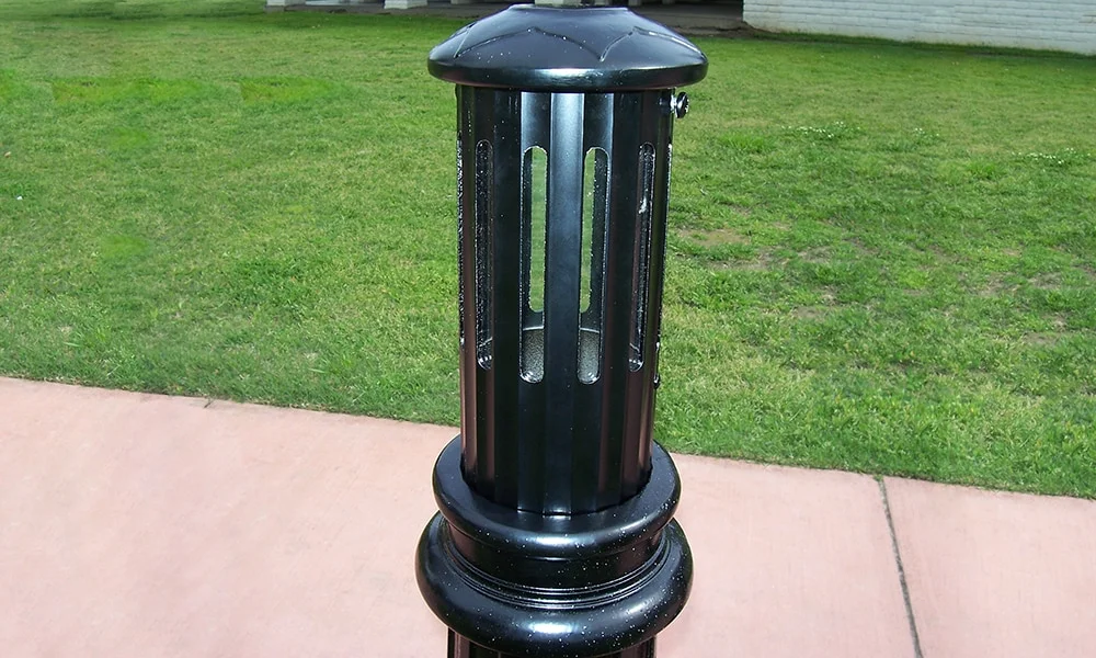Black cylindrical trash can on a sidewalk.