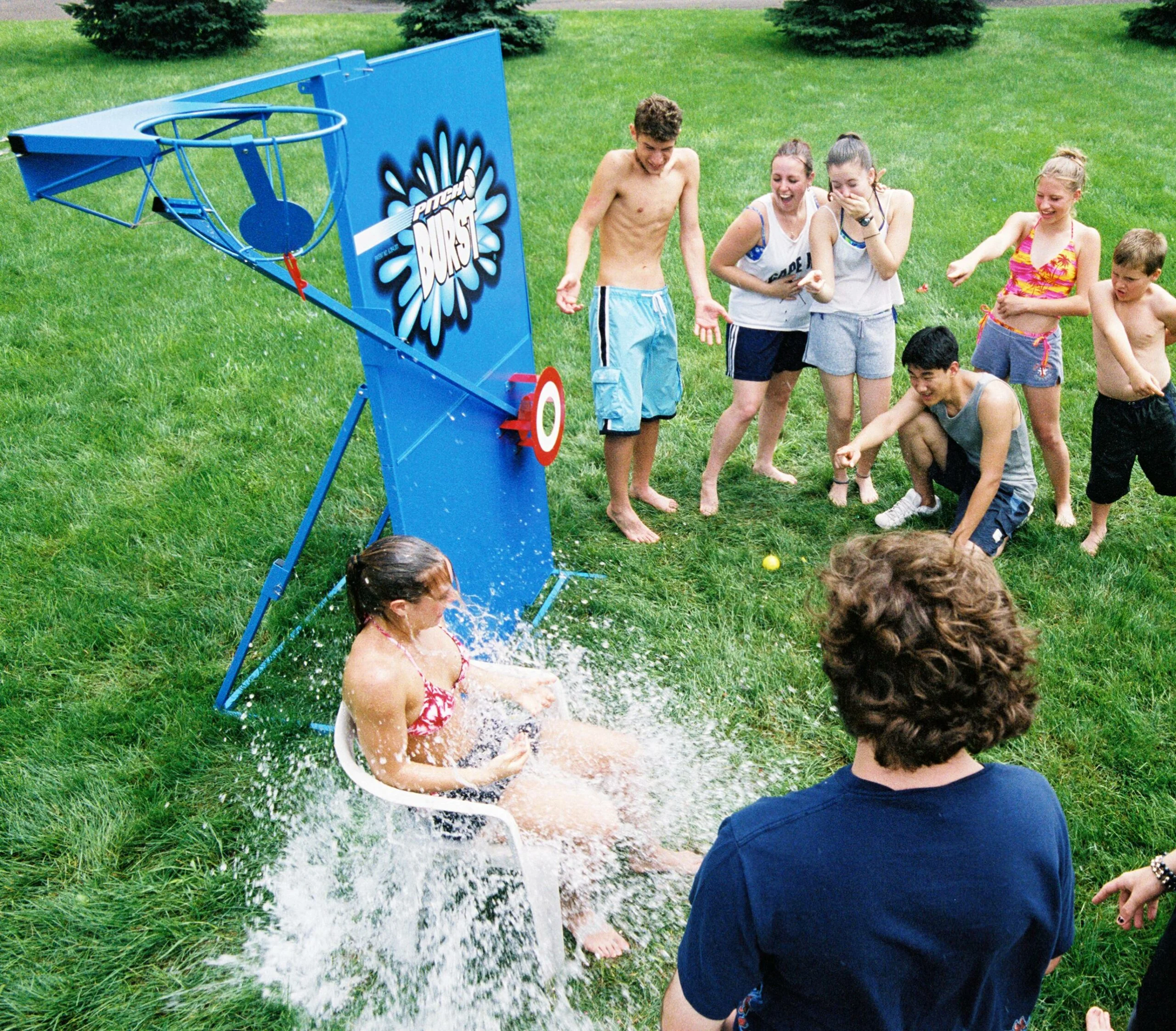 Girl sliding down a water slide while others watch.