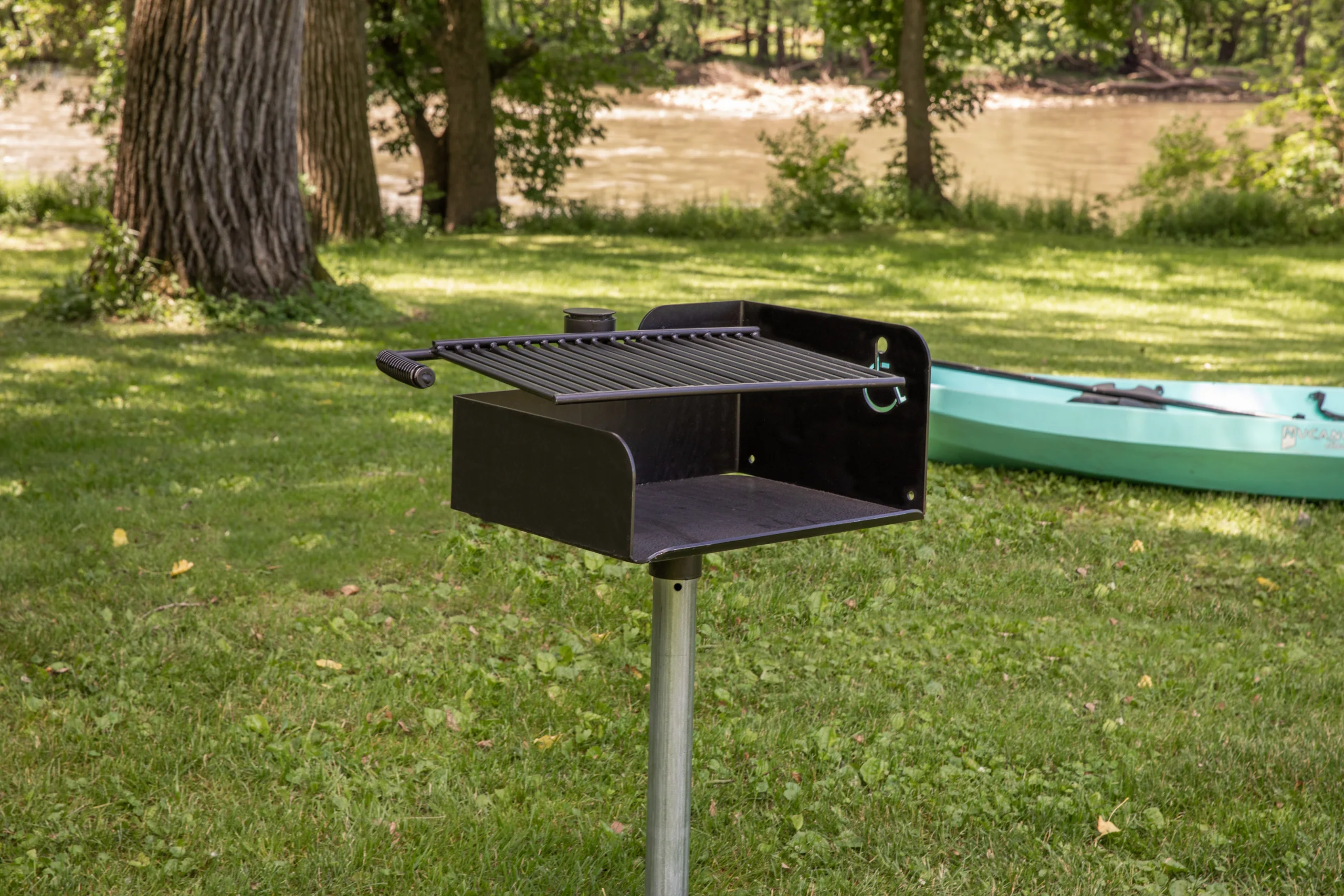 Portable grill on grass near a river.