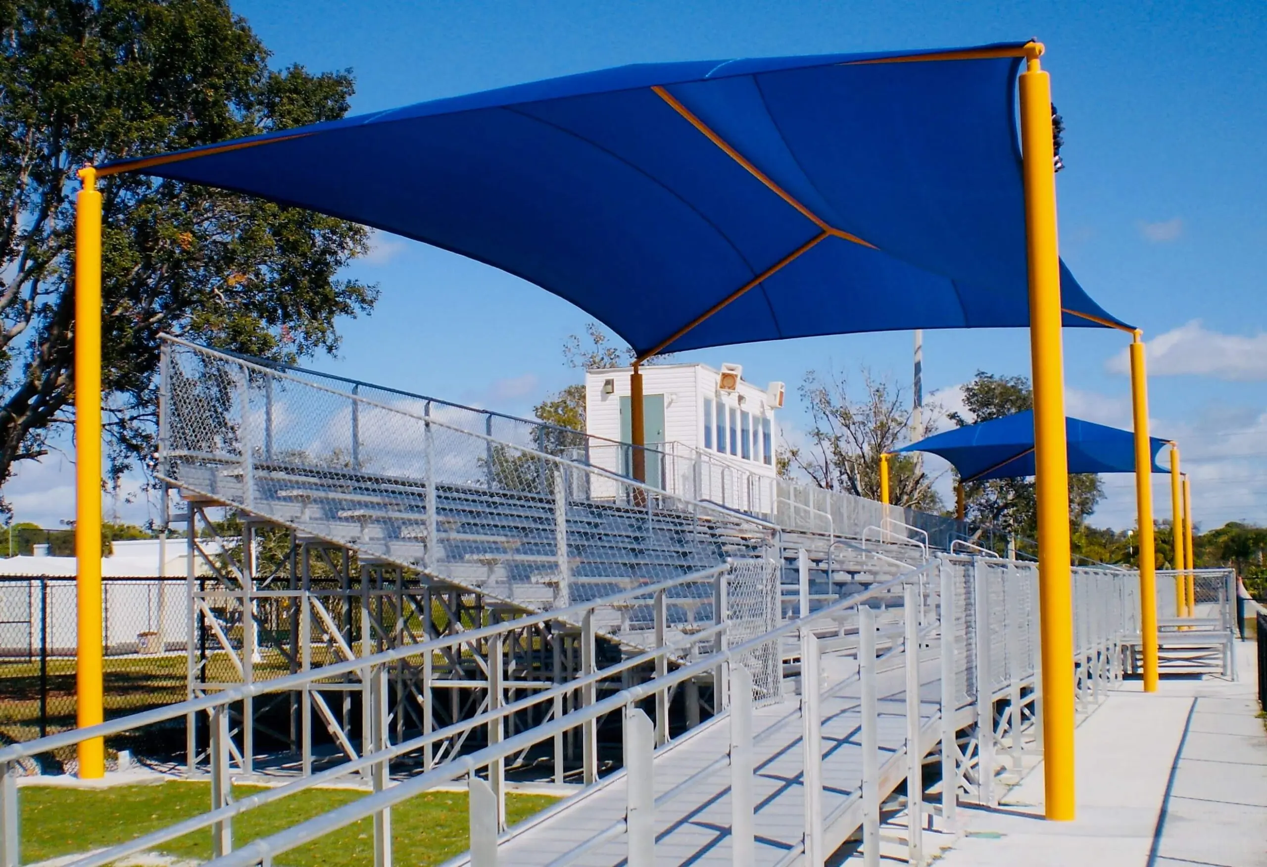 Outdoor bleachers with blue shade sails and yellow poles.