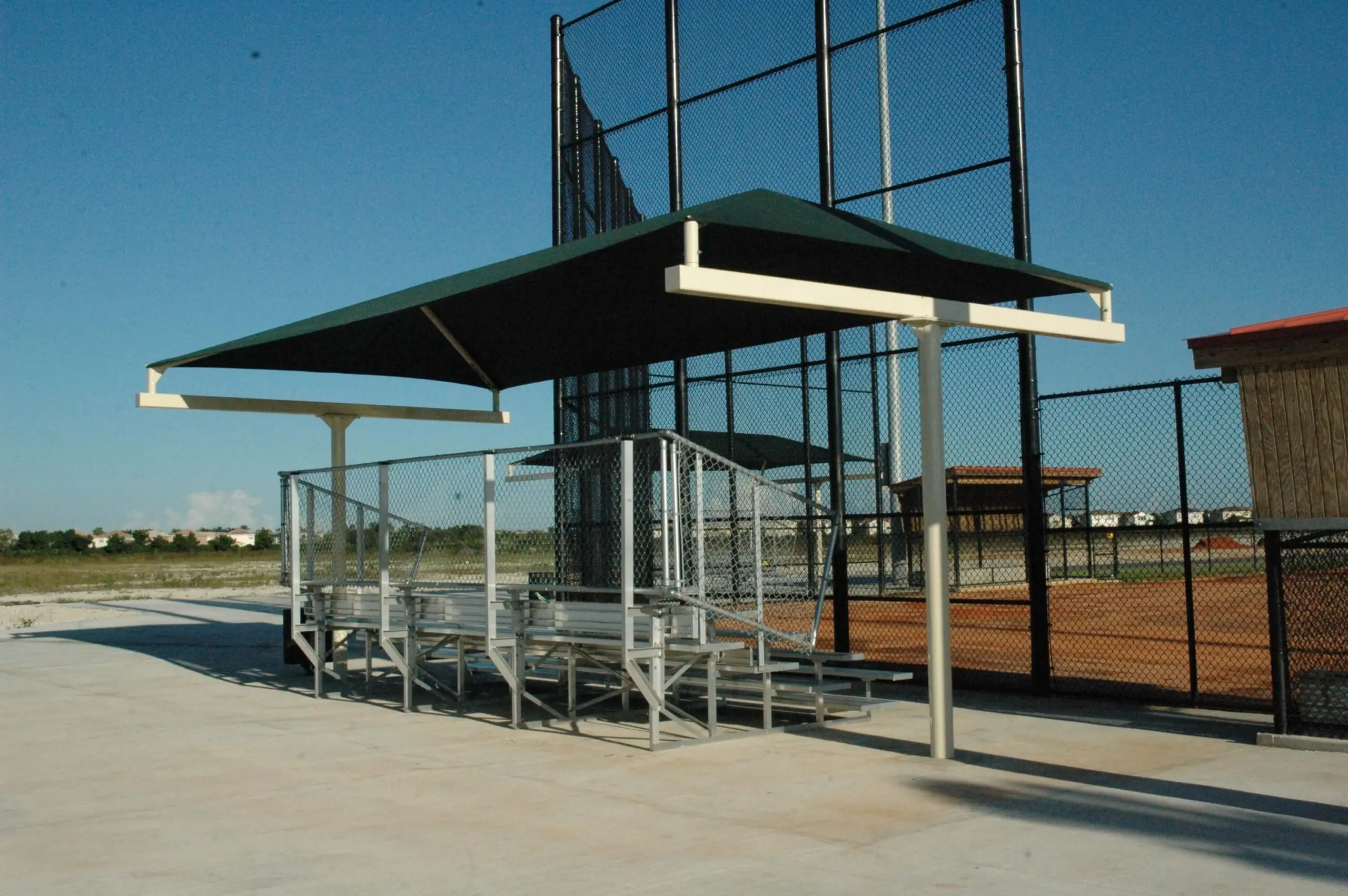 Baseball dugout with green roof and metal seating.