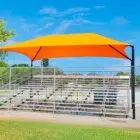 Orange and yellow shade sail over bleachers at a sports field.