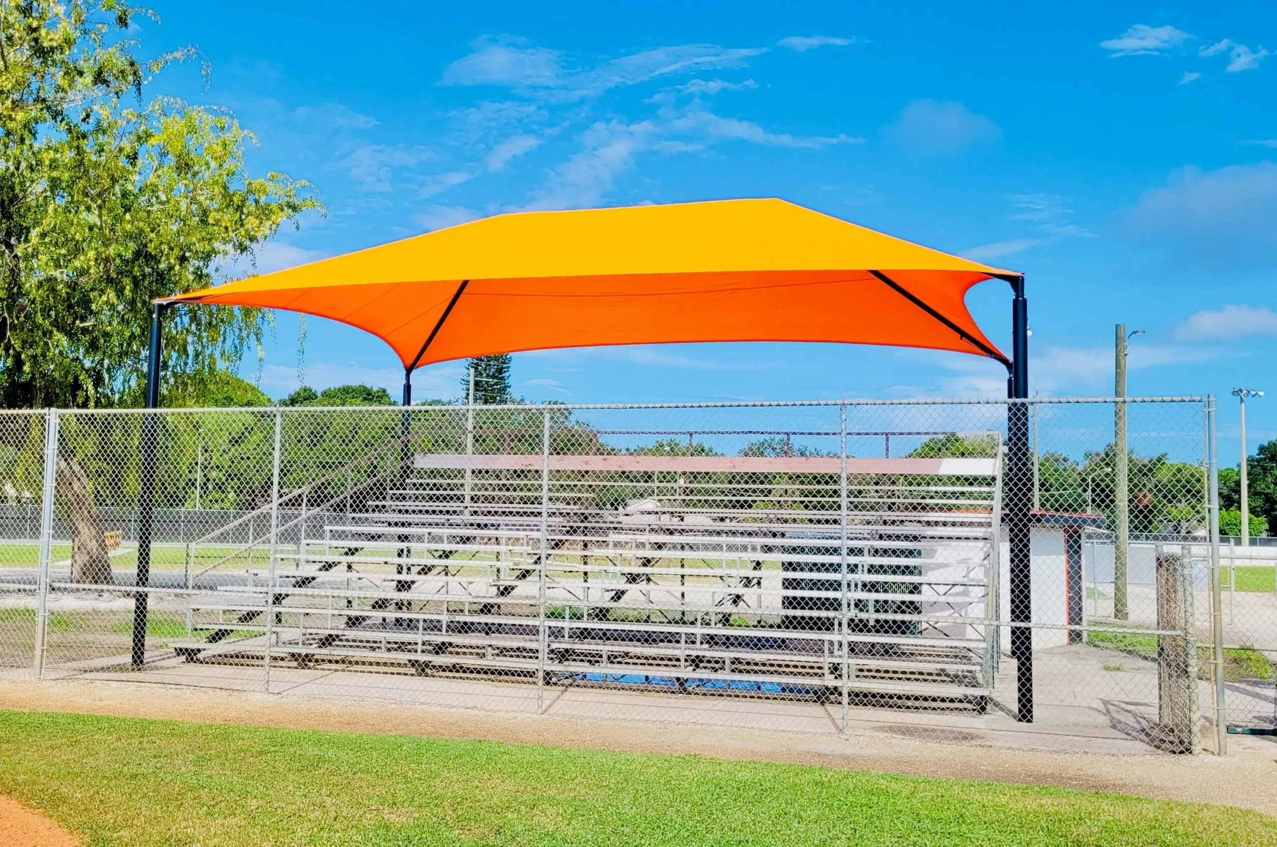 1BB-5-HD-10-PR-scaled-1 Orange and yellow shade sail over bleachers at a sports field.