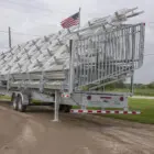 Trailer carrying a stack of metal ladders on a dirt road.