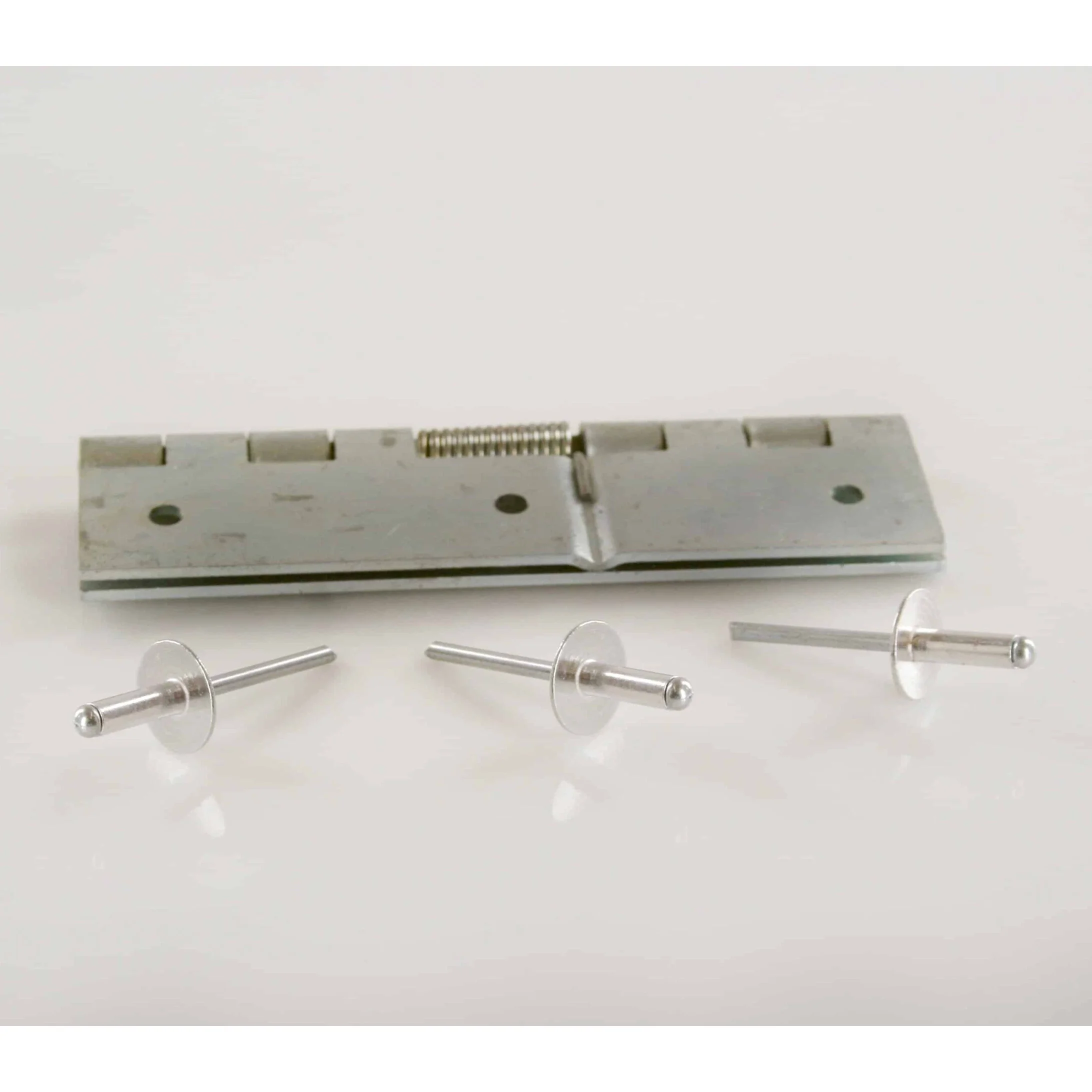 Metal rivet tool and two metal rivets on a white surface.