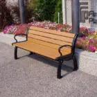 Wooden bench on a sidewalk near flowers.