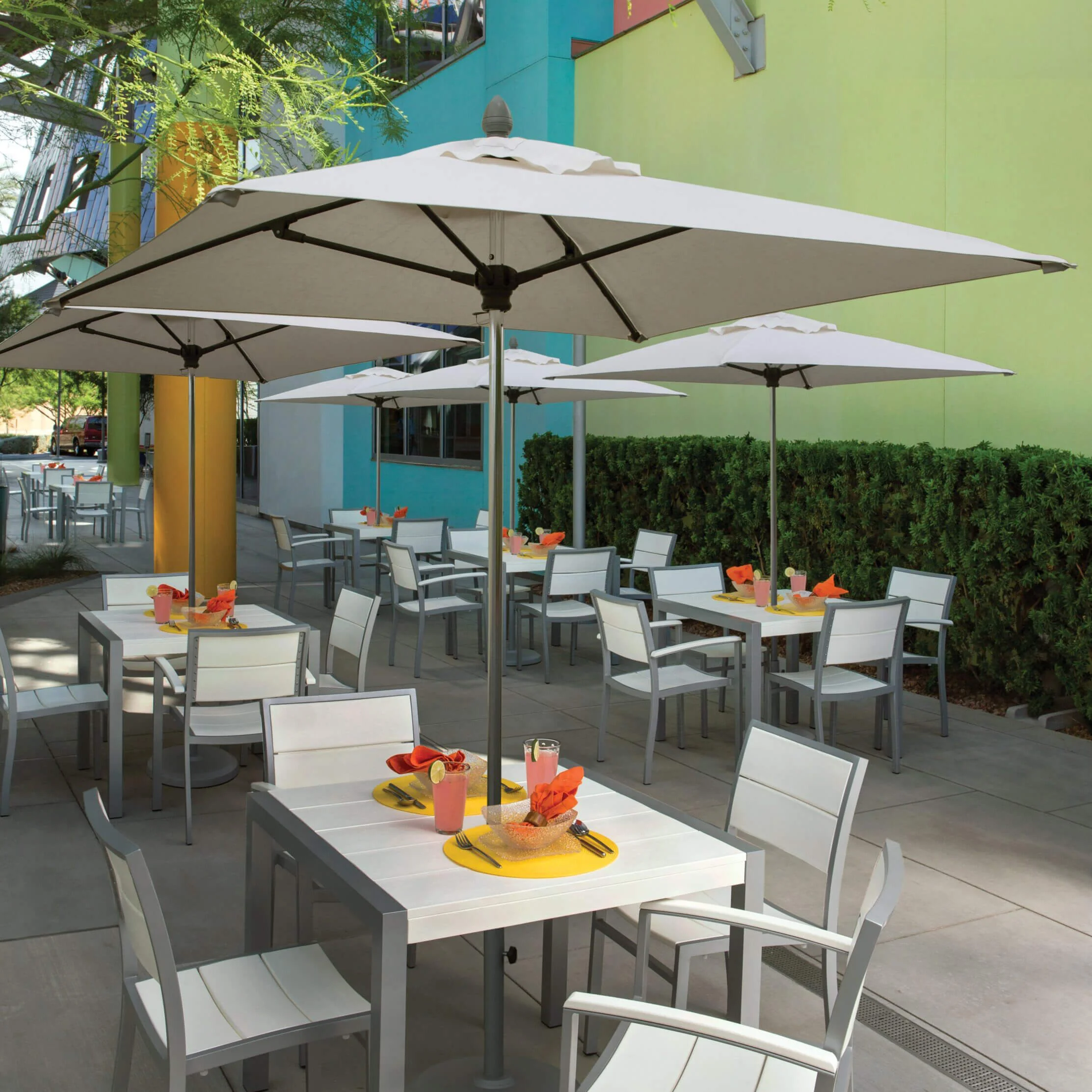 Lucaya-6ft-Sq-Environmental-scaled-1 Outdoor patio furniture set with white tables and chairs under large umbrellas.