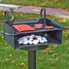 Portable grill with hot dogs and cookies cooking on a grassy outdoor area.