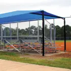 Baseball dugout shelter with blue roof and metal bleachers.