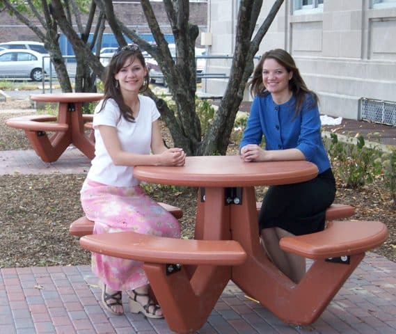 Two women sitting at a red picnic table outdoors.