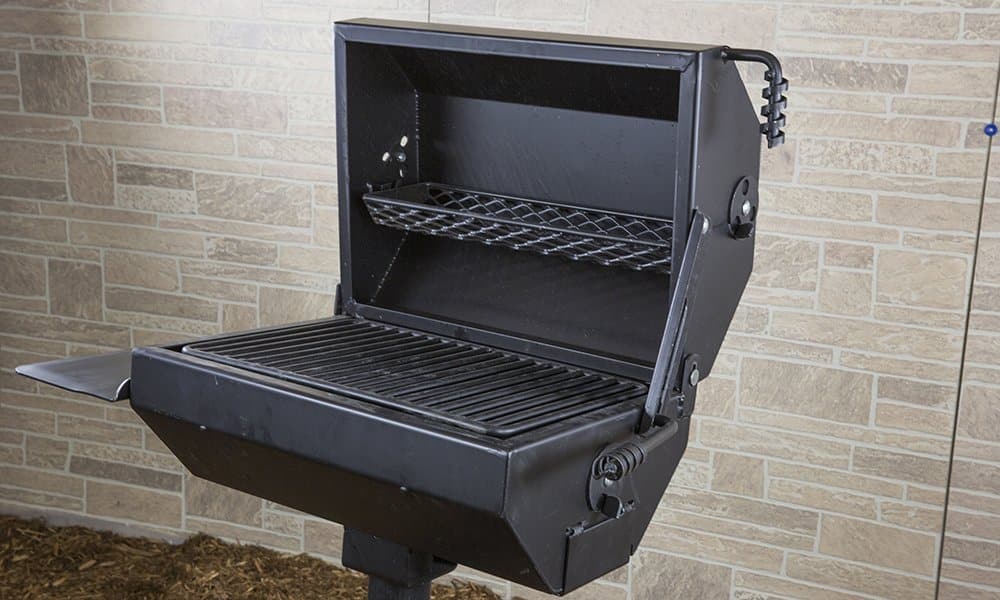 Outdoor grill with open lid and shelf against brick wall.