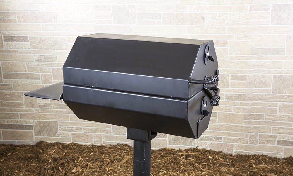Black electric grill on a stand in front of a brick wall.