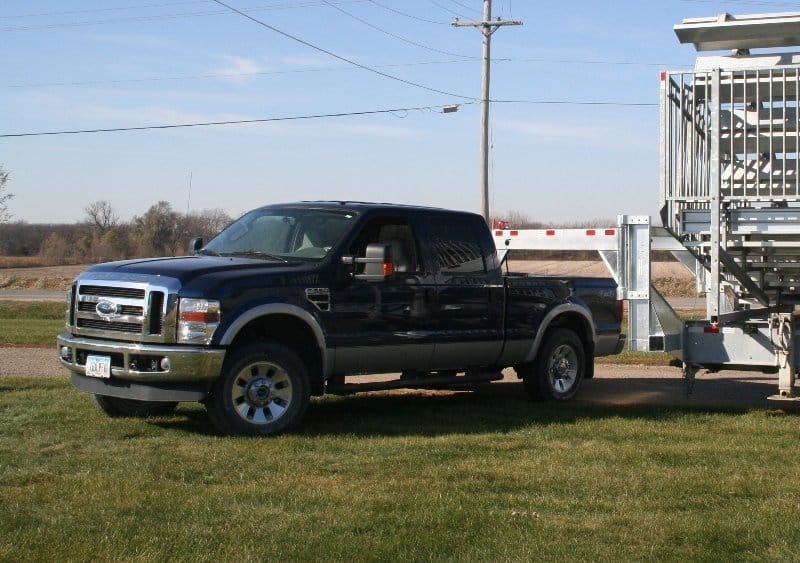 Black pickup truck parked on grass next to a trailer.