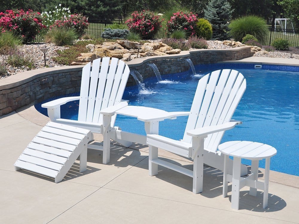 White Adirondack chairs and side table by a pool.