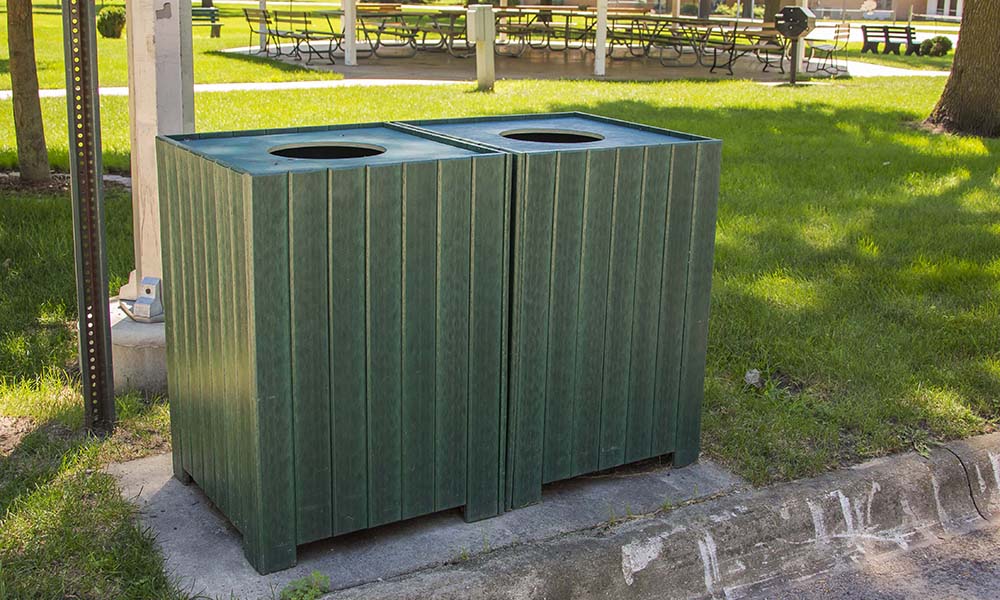 Green trash bin in a park setting.