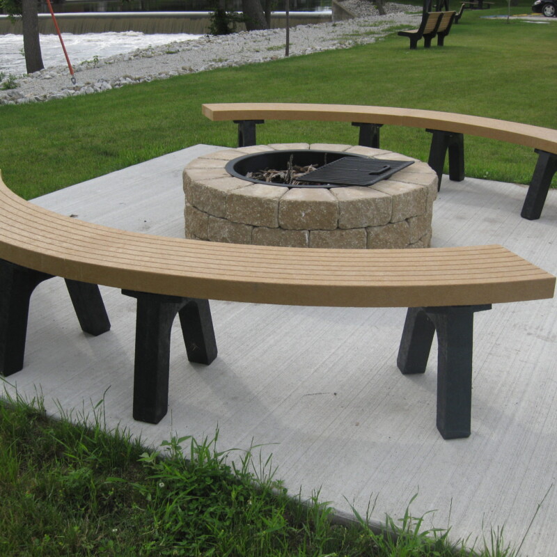 Outdoor curved bench and fire pit in a park setting.