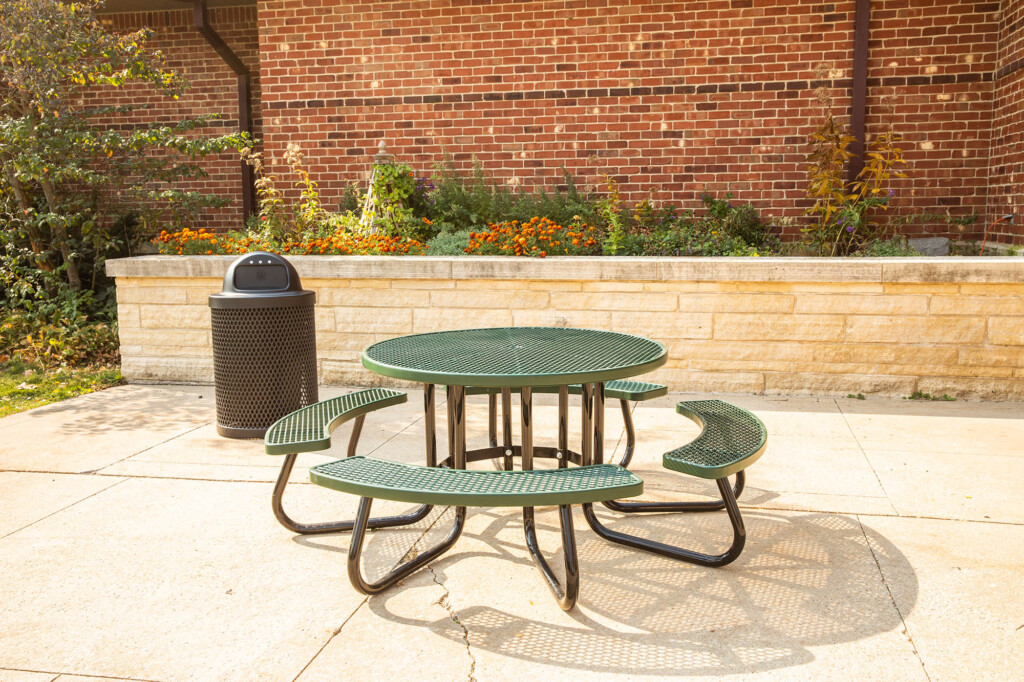 Outdoor green metal picnic table and benches in front of a brick building.