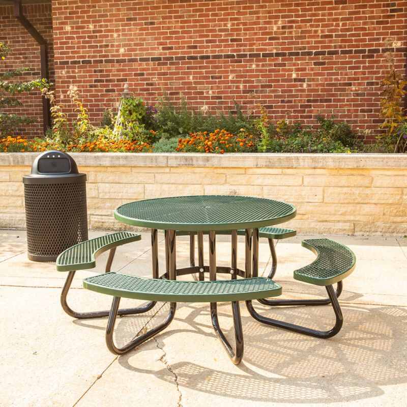 Outdoor green metal picnic table and benches in front of a brick building.