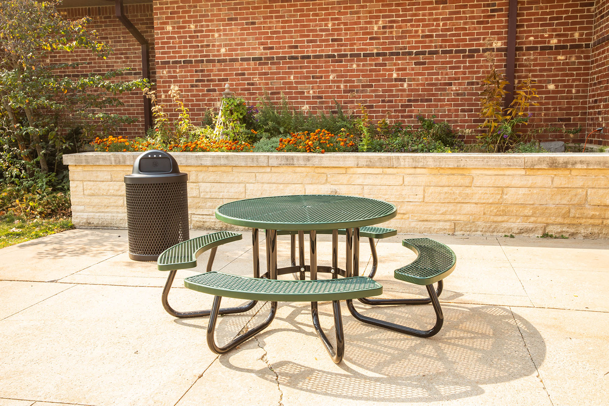 Outdoor green metal picnic table and benches in front of a brick building.
