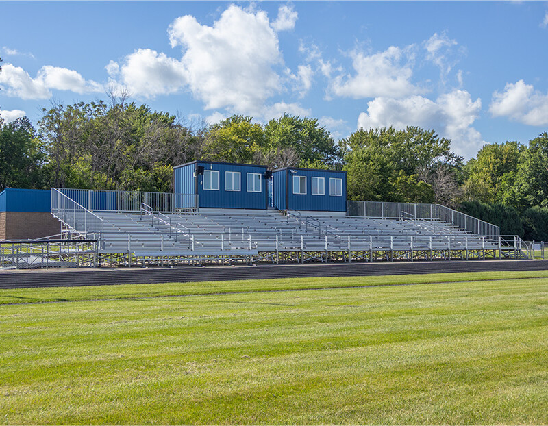 Football field with bleachers and trees in background.