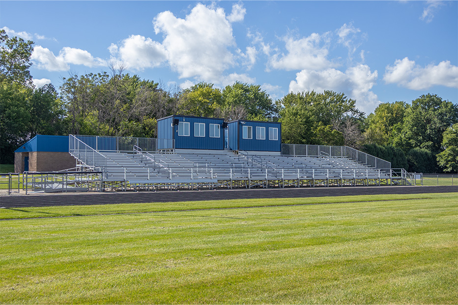Football field with bleachers and trees in background.