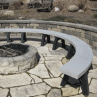 Outdoor stone fire pit and curved bench in a garden setting.