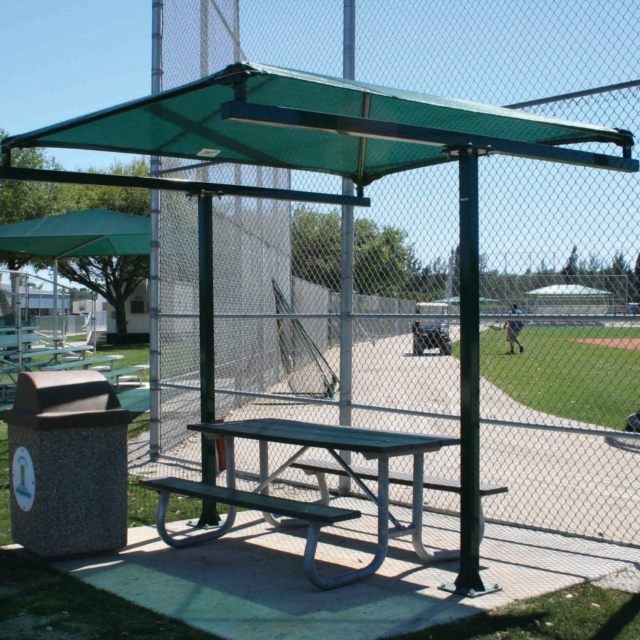 t-style_ballpark_rainforest_fortmyers Baseball field shelter with picnic table and trash can.